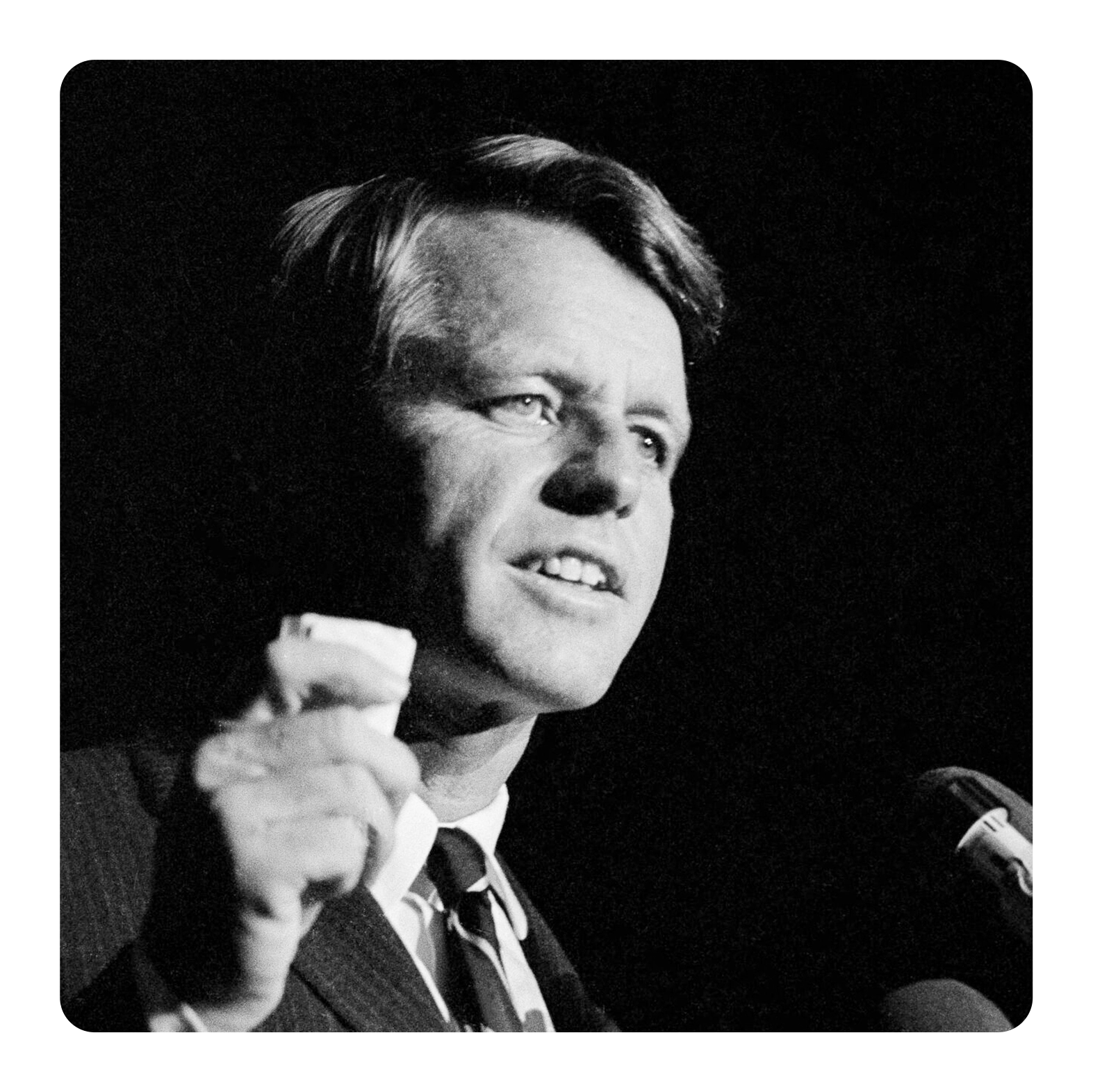 Archival image of Robert F Kennedy delivering a speech. The image is rendered in a stark black and white.